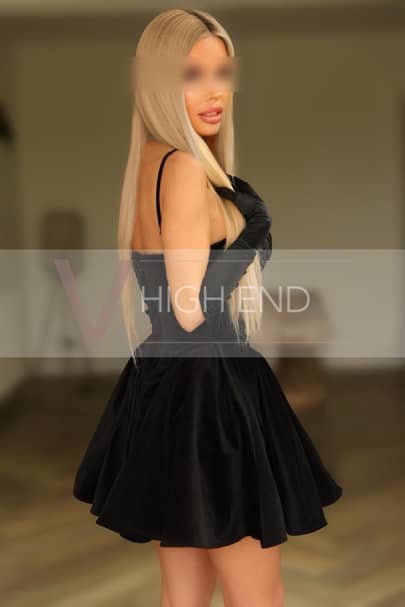 Tall elite model Noemi is gently touching her blonde locks in a black dress