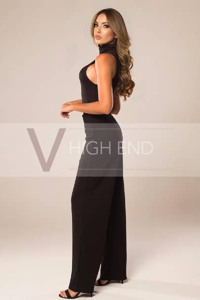 Elite escort is wearing black elegant trousers and turtleneck top, black high heels sandals