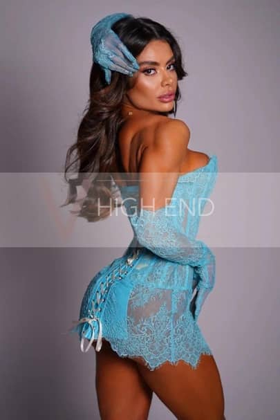 Hailey a Gloucester Road escort wearing a blue lacy corset and touching her hair gracefully