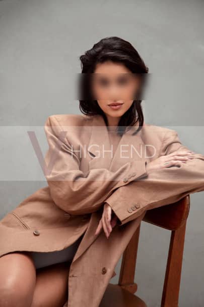 Elite model Nina sitting on a chair, dressed in a beige jacket