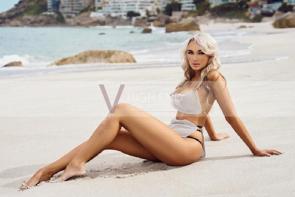 London escort Athena is sitting on the beach in a sexy tiny silver outifit