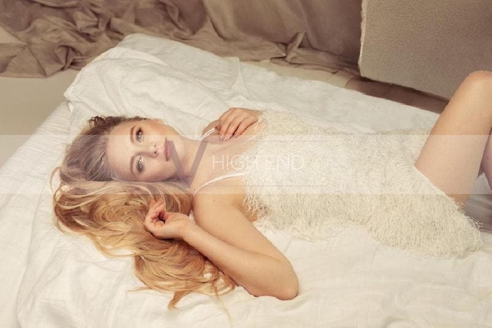 Luxury escort Lilian is lying on the bed in a white furry dress