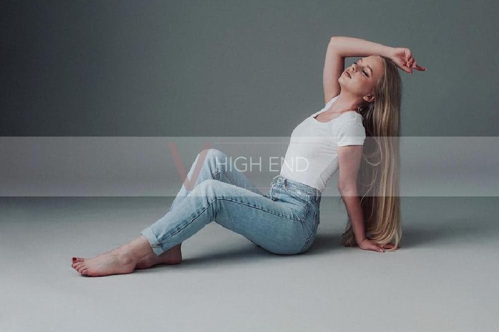 Blonde escort Liliana is sitting on the floor in jeans and simple white t-shirt