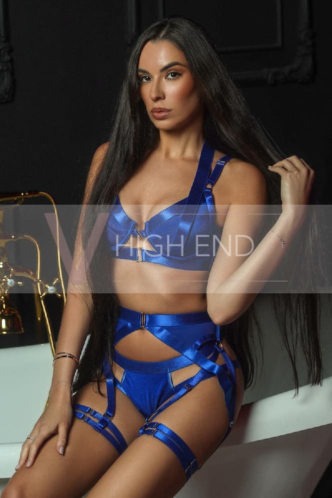 Agata is touching her brunette hair white leaning on edge of the bath in cobalt lingerie