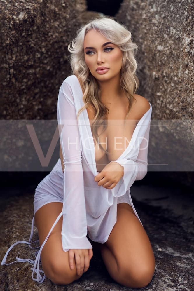High End companion Athena is kneeling on the beach showing off her cleavage