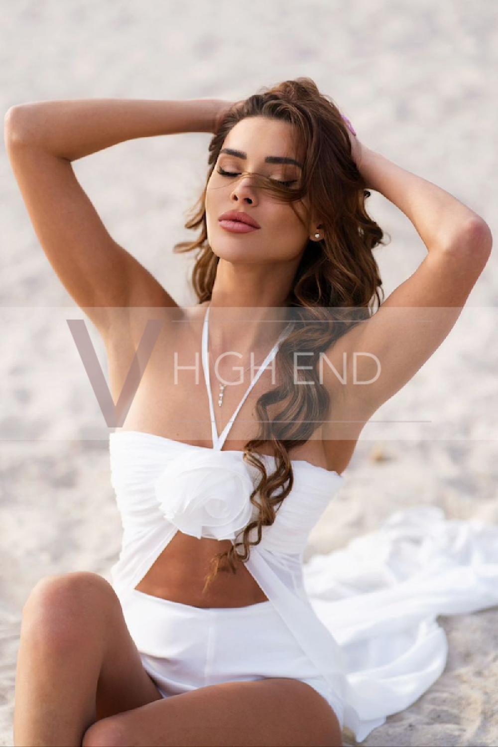 Brunette escort Ilona is posing on the beach in a white attire with her eyes close